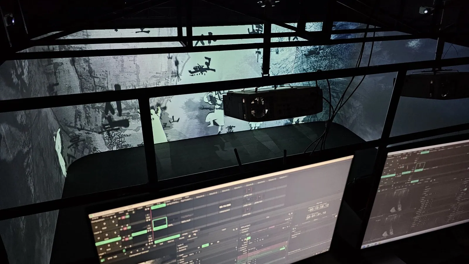 A projector hung from the truss above the screens, with the playout monitors in the foreground.