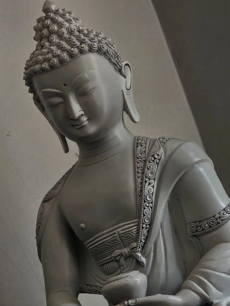 Close-up of the statue in a matte grey finish: the face, hair curls, the ornamented robe border and the alms bowl.