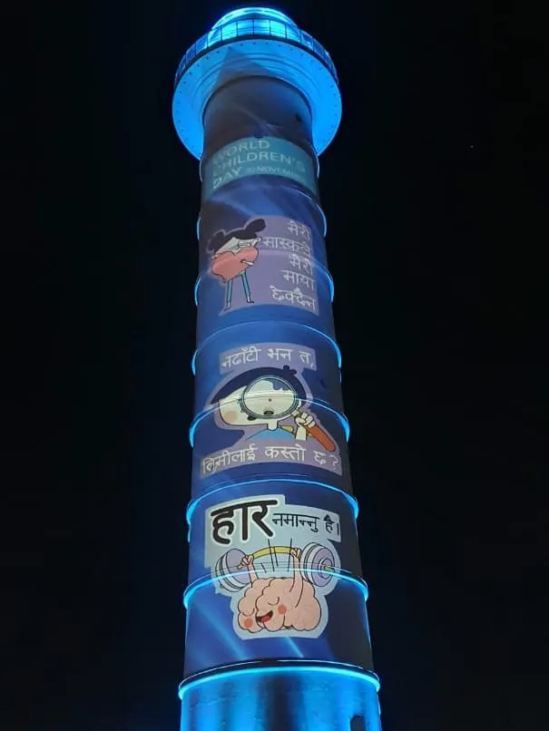 The tower in blue light with World Children's Day and Nepali cartoon panels about caring for your mind projected down the shaft.