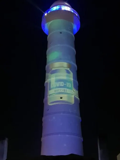 The tower in blue light with a large COVID-19 vaccine bottle projected on its shaft.