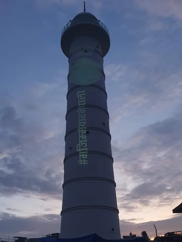 The tower at dusk with a green hashtag and a circular graphic projected on its shaft under a blue and pink sky.