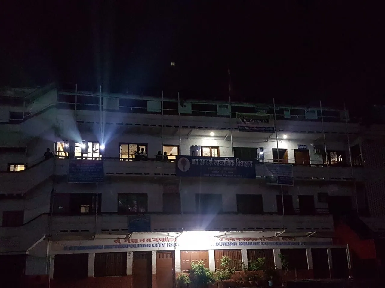 Night photograph of the building across the square, with projector beams visible from an upper-floor window.