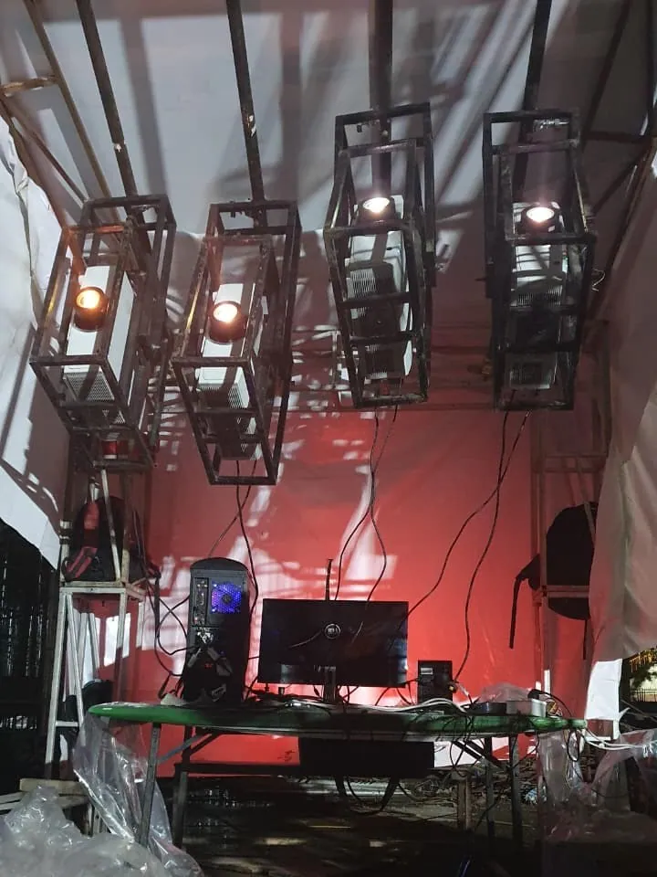 Four projectors hung in steel cages from a tent frame, with a table and a computer under them.