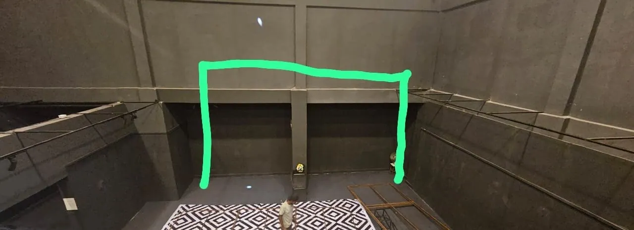 The empty dark hall seen from a platform, with a green outline drawn over the photo and a black and white printed sheet on the floor.